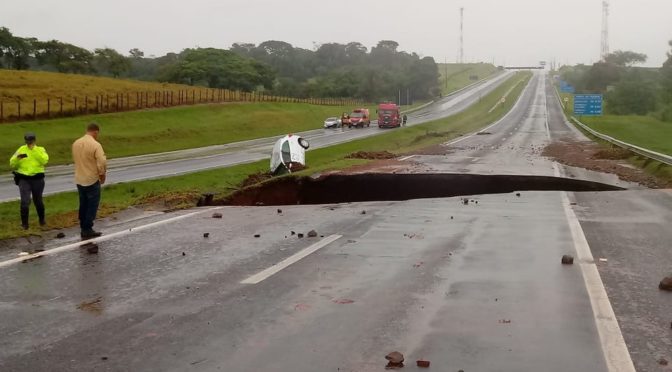 Equipes de resgate fazem buscas por caminhão que sumiu ao cair em cratera aberta em rodovia durante chuva